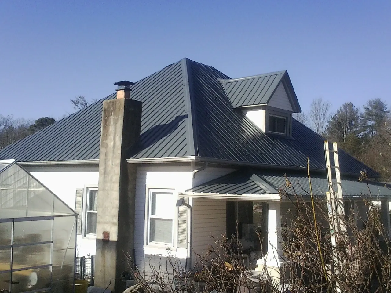 Dark blue standing seam metal roof on a white farmhouse with dormer — Slate & Tile Roof Repair by Roofing Brothers in Weslaco