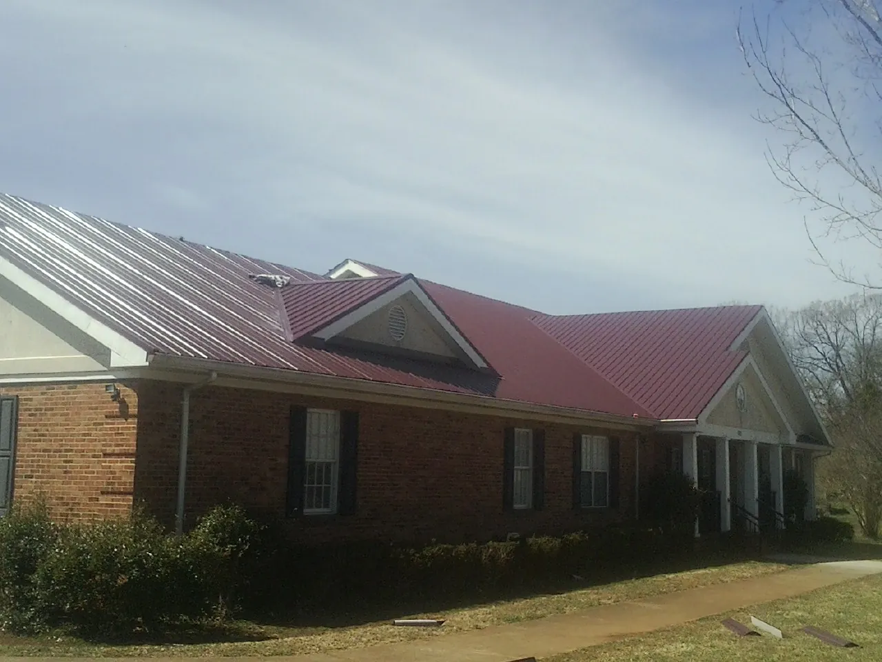 Red metal roof with gabled entries on a long brick building, from a Hail Damage Roof Repair job in Weslaco