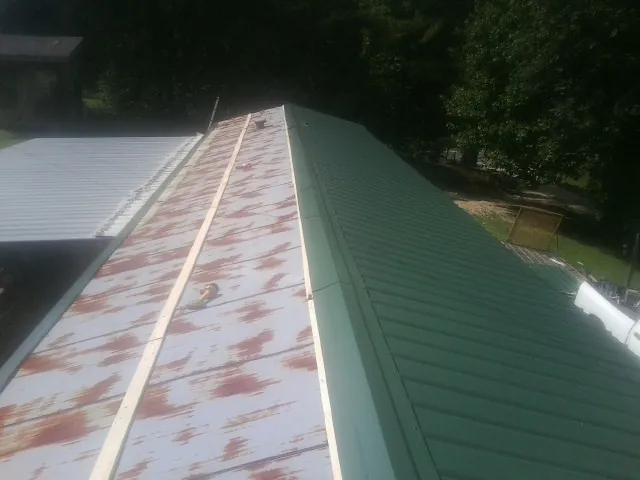 Old rusted panels beside newly installed green metal roofing — Wind Damage Roof Repair by Roofing Brothers in Weslaco