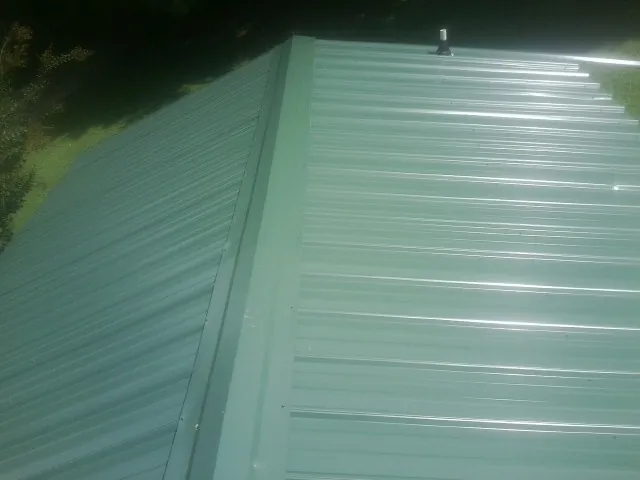 New green metal panels meeting at the ridge of a roof — Flat Roof Repair work by our crew in Weslaco