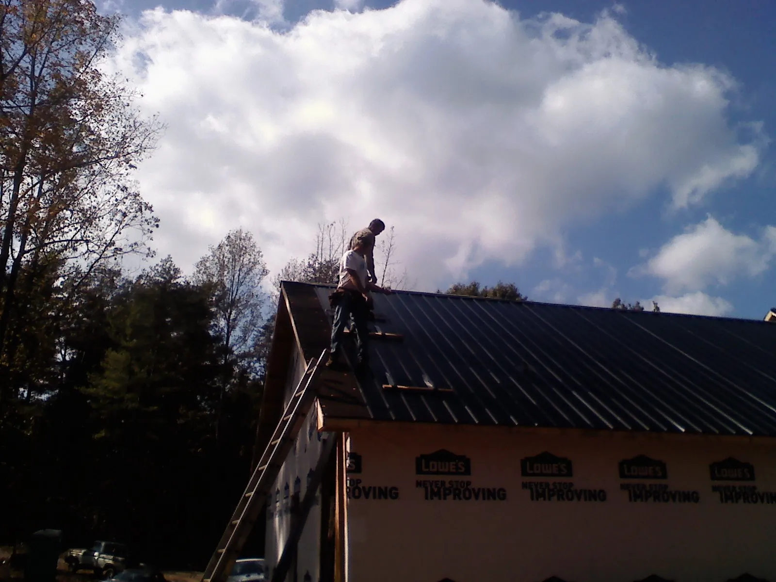 Roofer fastening dark metal panels high against a cloudy sky, from a Roof Inspection job in Weslaco