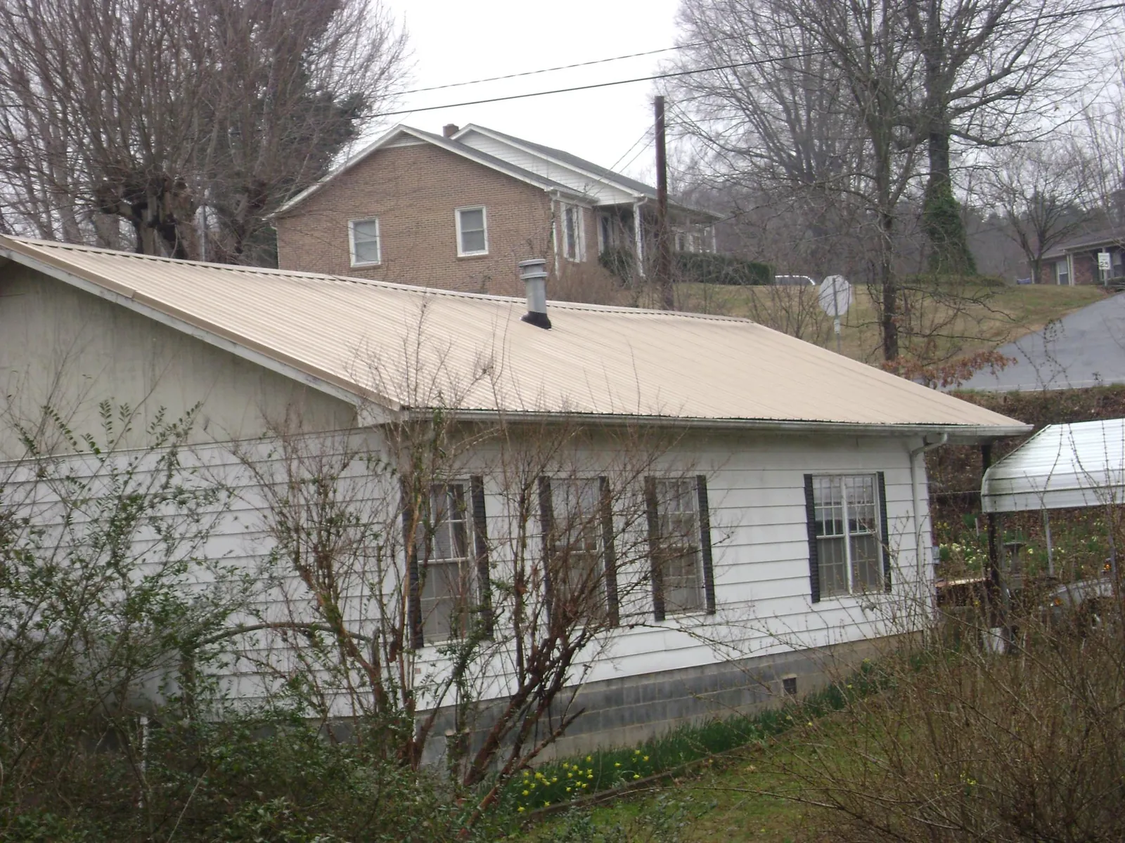 Tan metal roof on a white sided house set into a hillside — Commercial Roofing by Roofing Brothers in Weslaco